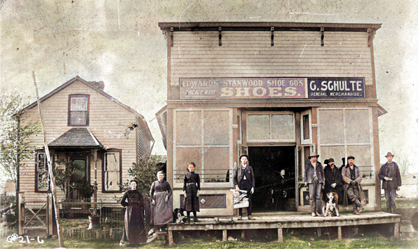 Latter 1800s people posed in front of G Schulte General Merchandise Store, colorized image